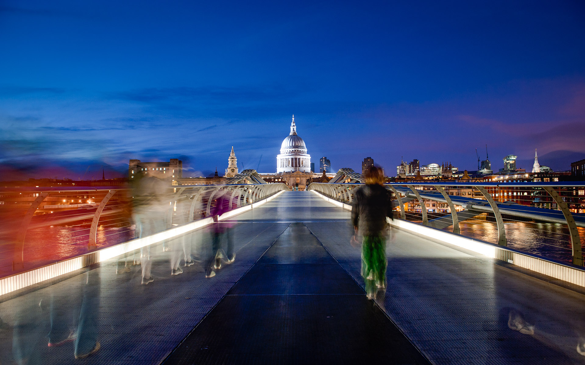 Low light night shot people walking across Millennium Bridge towards St Pauls Cathedral London England